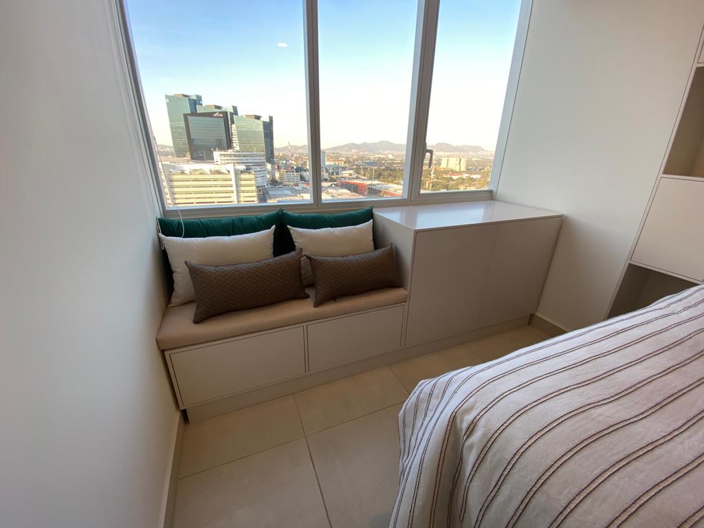 Banca con cajoneras a medida junto a ventana con vista a la ciudad, ideal para espacios pequeños.